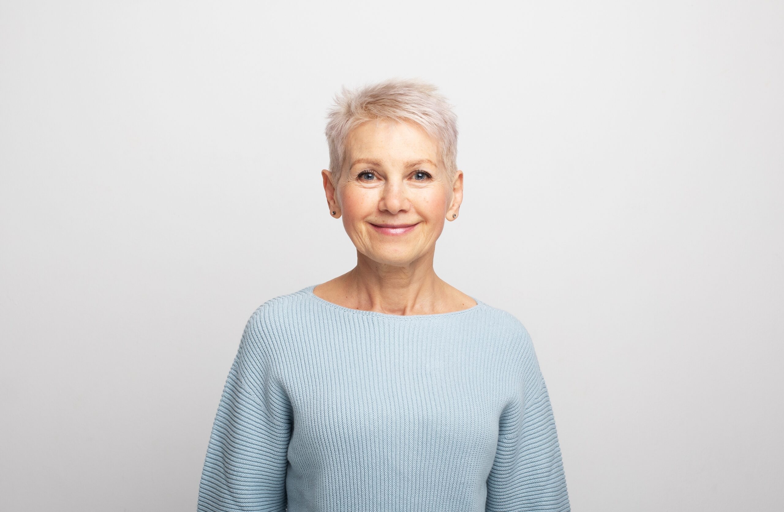 woman with a short pixie haircut in a blue sweater on a gray background